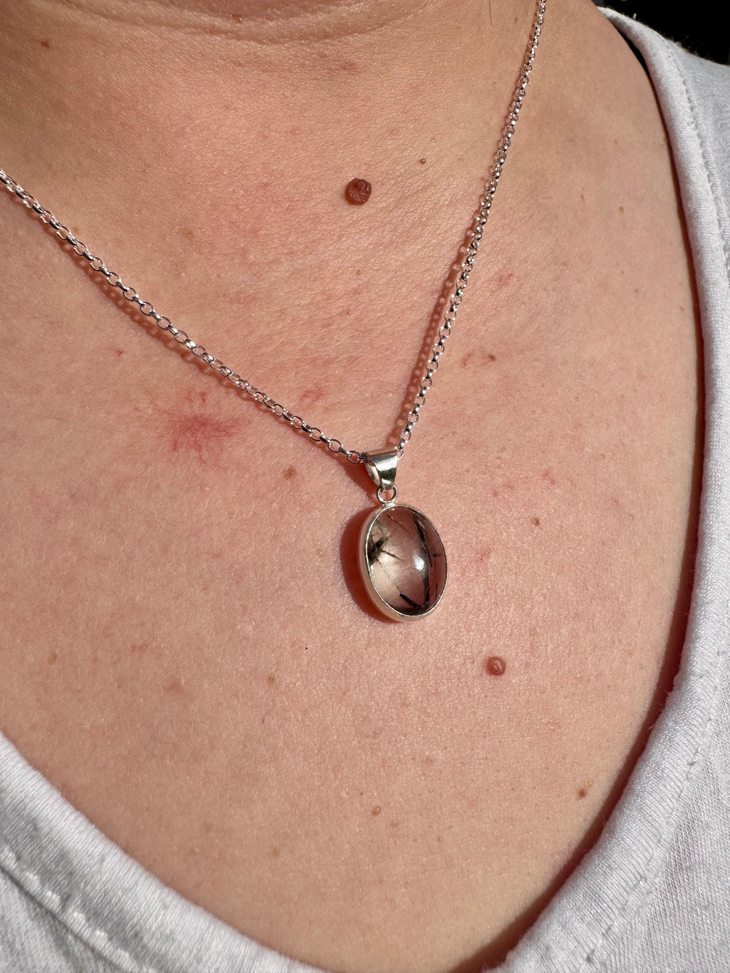 A close-up of a person's chest wearing a silver chain necklace with an oval clear and black quartz pendant.