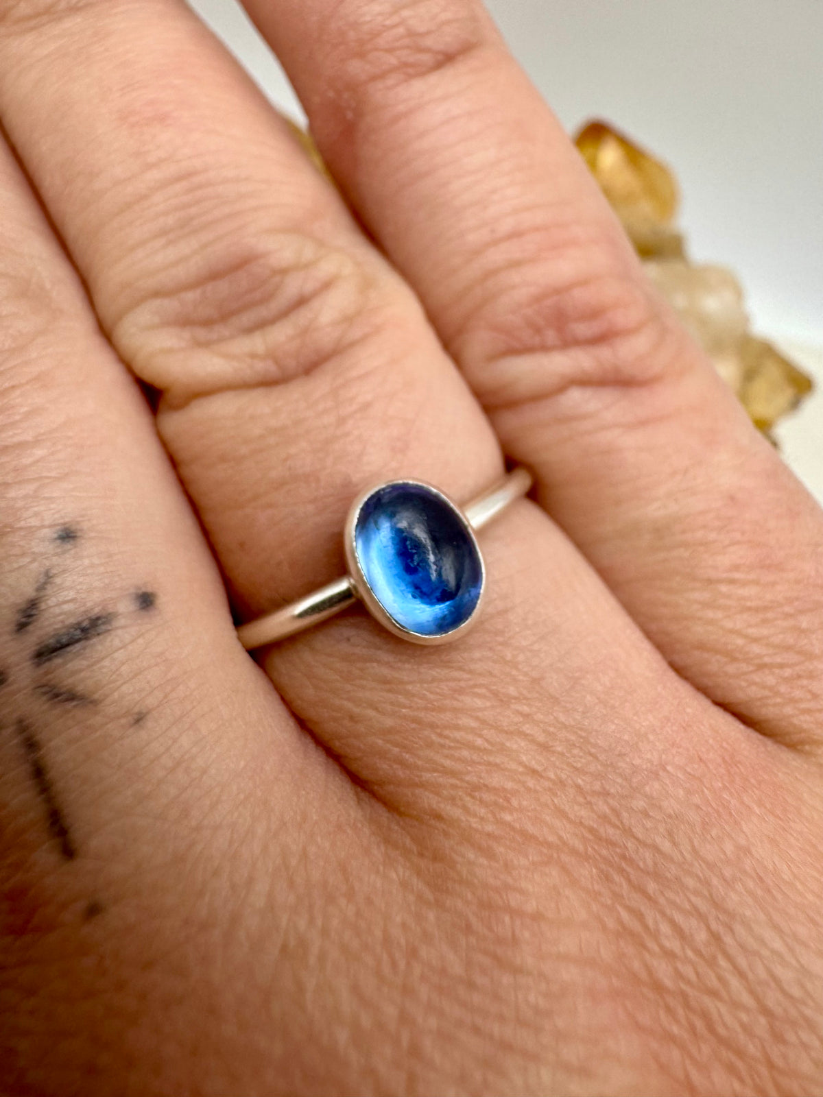 A silver ring with an oval blue iolite cabochon gemstone worn on a person's finger, shown in a close-up shot.