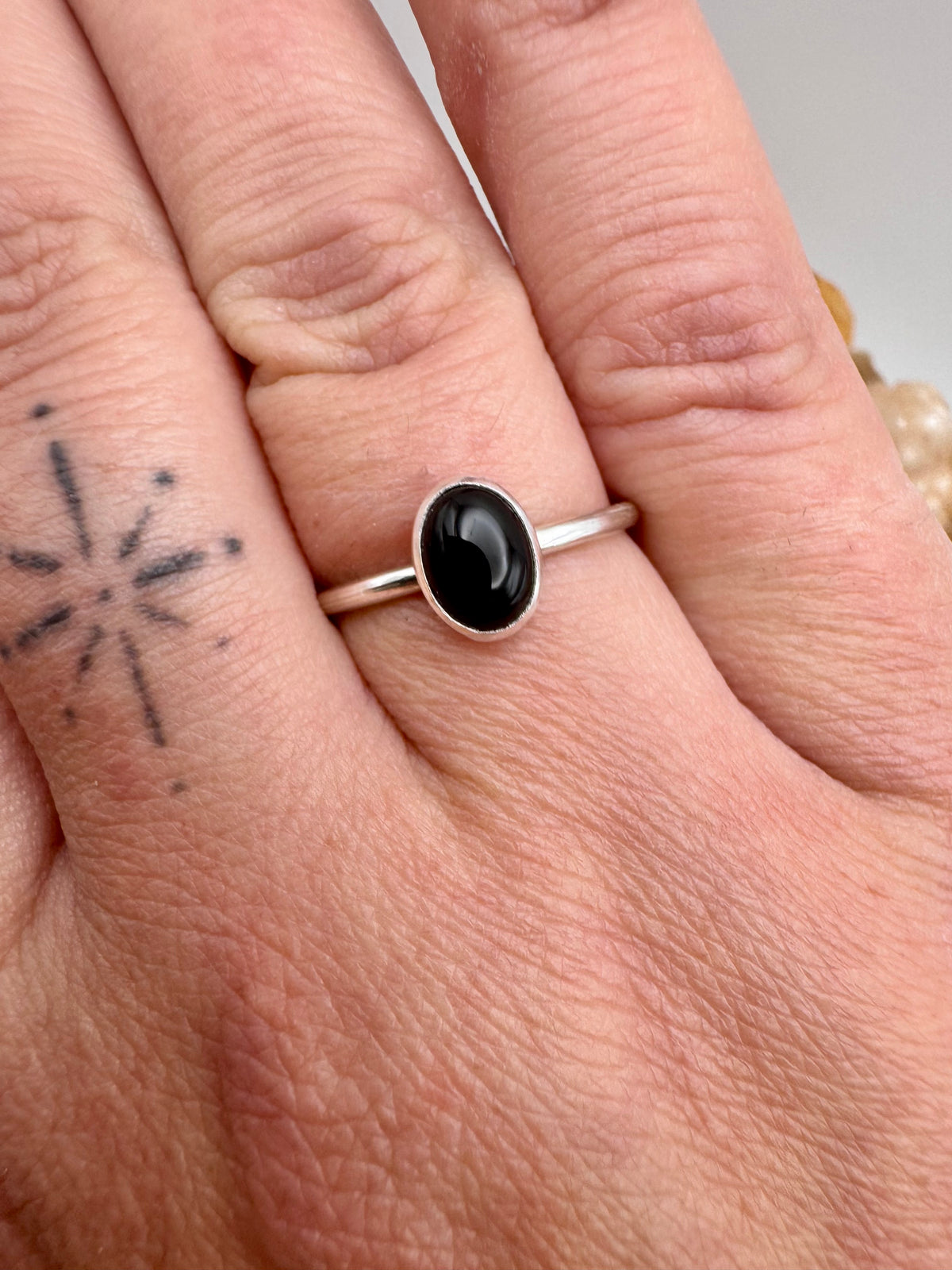 A silver ring with a smooth, oval onyx cabochon stone worn on a person's finger, shown in a close-up shot.