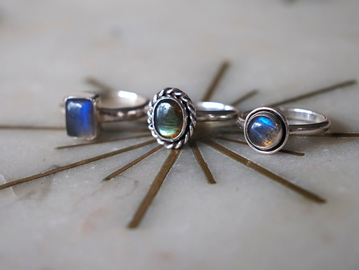 Three silver rings with iridescent blue and green labradorites arranged on a light stone surface with a decorative starburst prop.