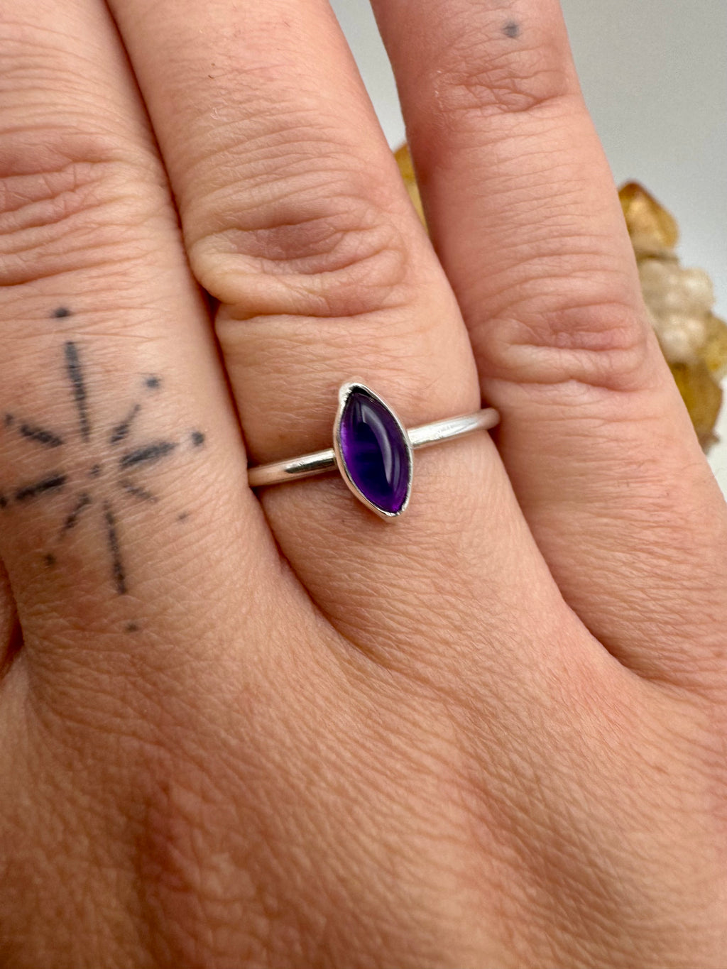 A silver stacking ring with a marquise-cut purple amethyst gemstone worn on a person's finger, shown in a close-up shot.