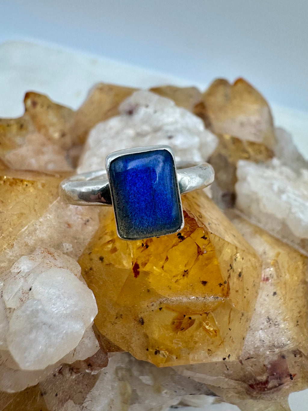 A silver ring with a rectangular, deep blue labradorite, displayed on a cluster of yellow and white crystals.