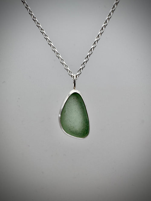 A silver chain necklace with a teardrop-shaped seafoam green sea glass pendant, open back for the light to shine through, displayed against a neutral gray background.