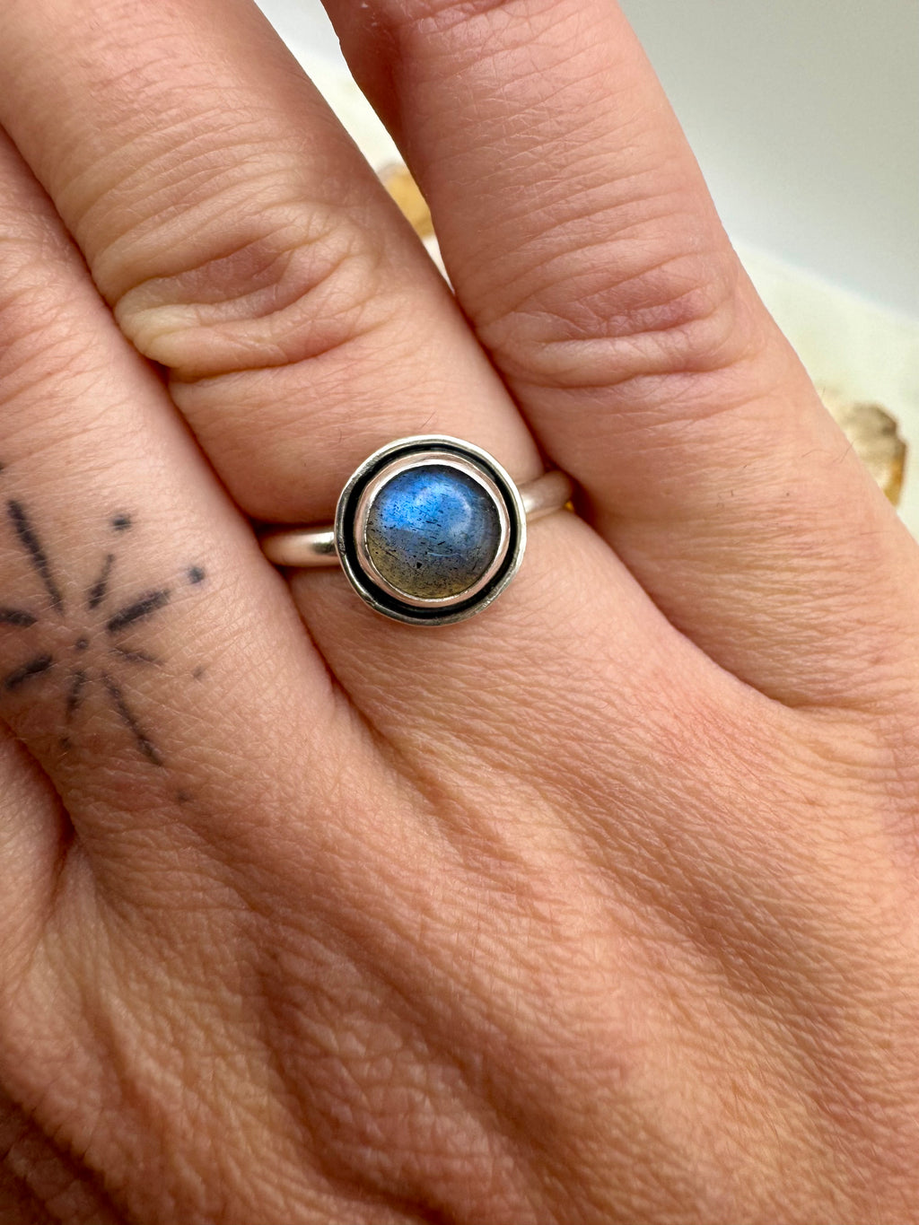 A sterling silver ring with a round bezel-set blue labradorite stone, shown worn on a person's finger.