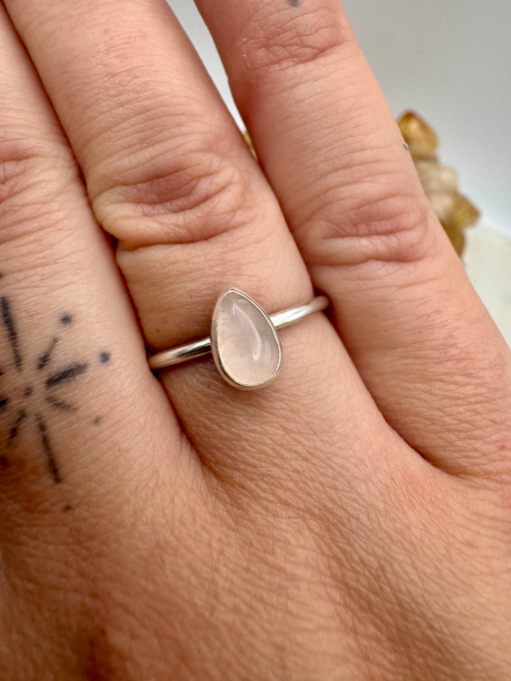 A silver stacking ring with a teardrop-shaped pale pink rose quartz stone, shown worn on a person's finger.