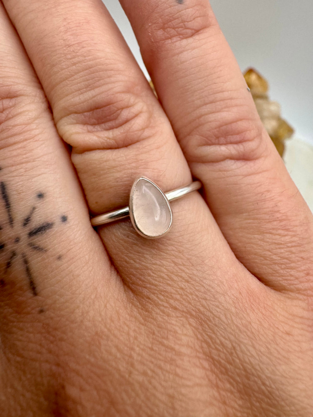 A silver stacking ring with a teardrop-shaped pale pink rose quartz stone, shown worn on a person's finger.