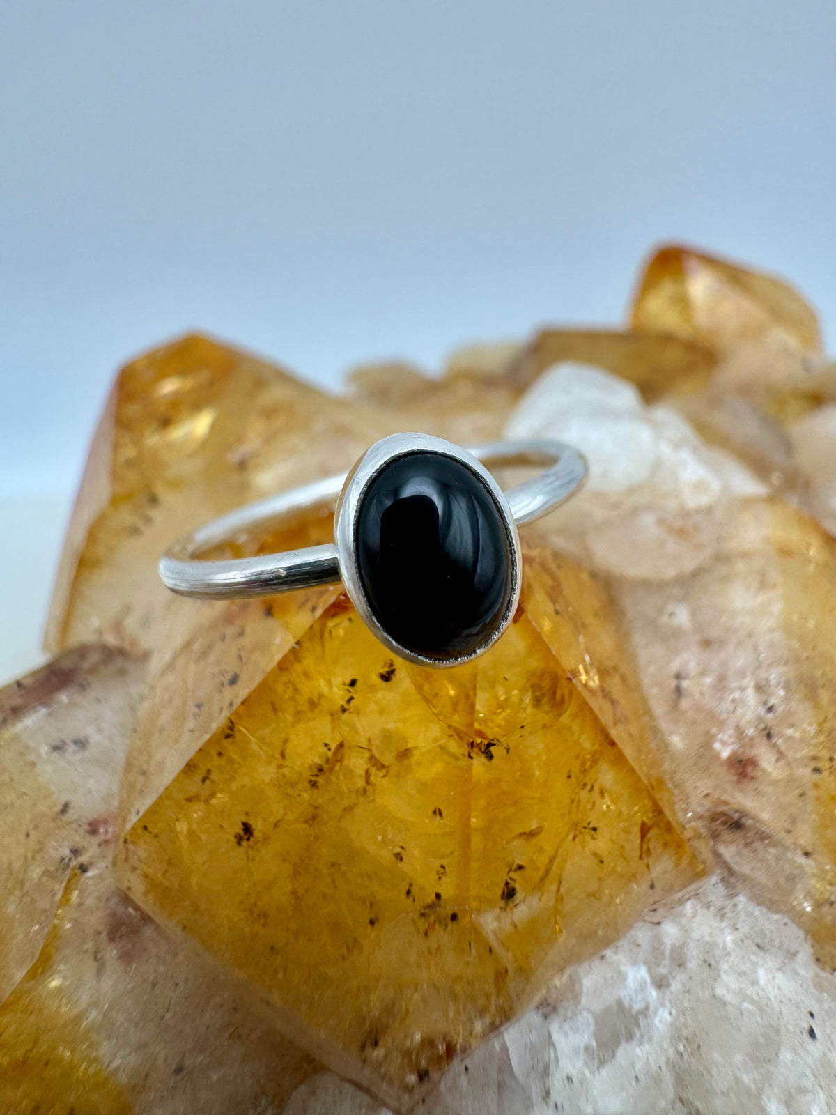 A sterling silver ring with a smooth, oval black onyx cabochon gemstone, displayed on a crystal cluster against a light gray background.