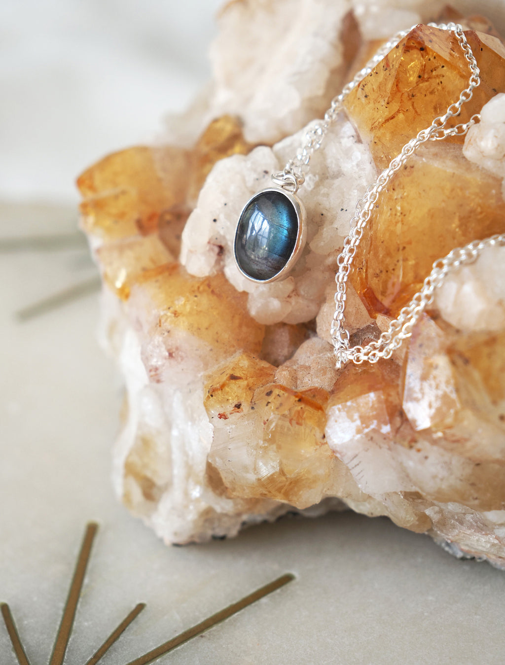 A silver chain necklace with an oval labradorite pendant resting on a crystal cluster.