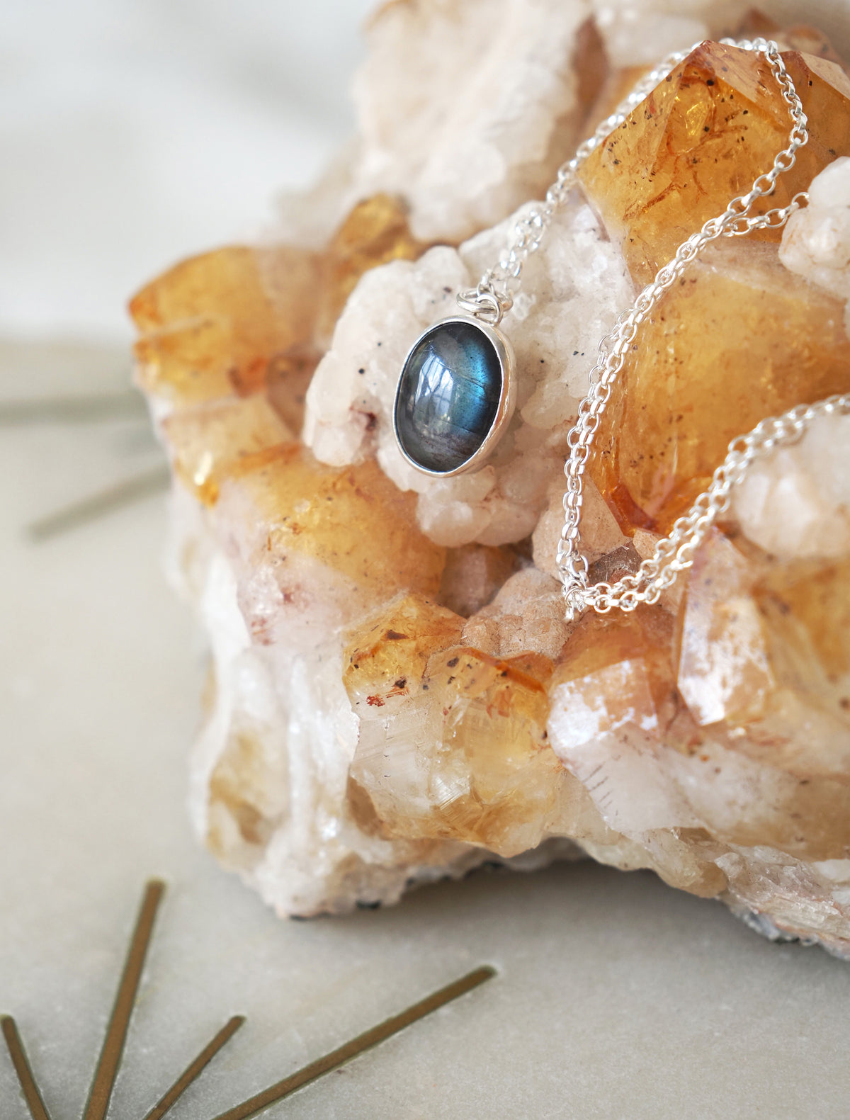 A silver chain necklace with an oval labradorite pendant resting on a crystal cluster.