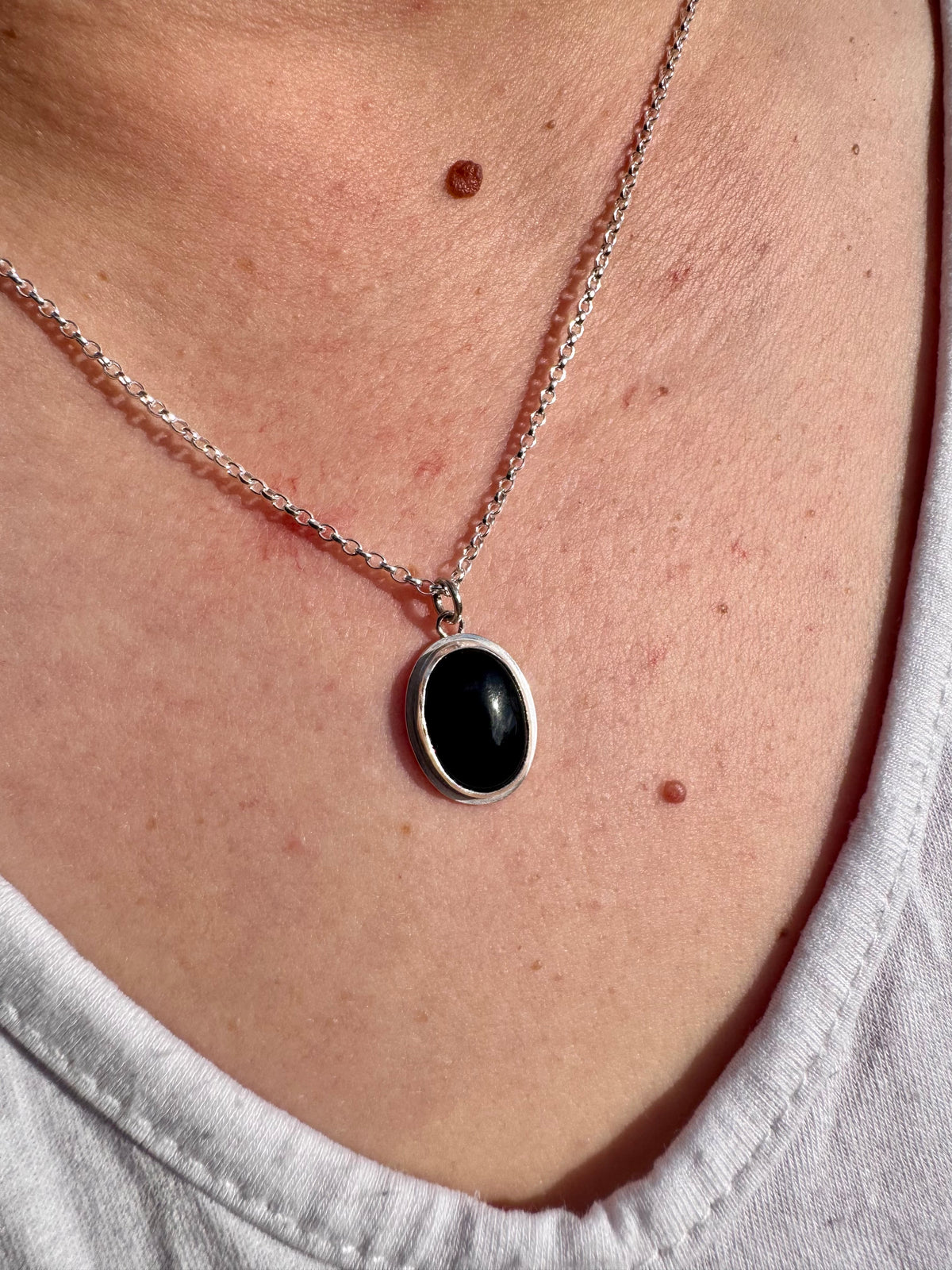 A close-up of a person's neck and chest wearing a silver chain necklace with an oval onyx pendant.