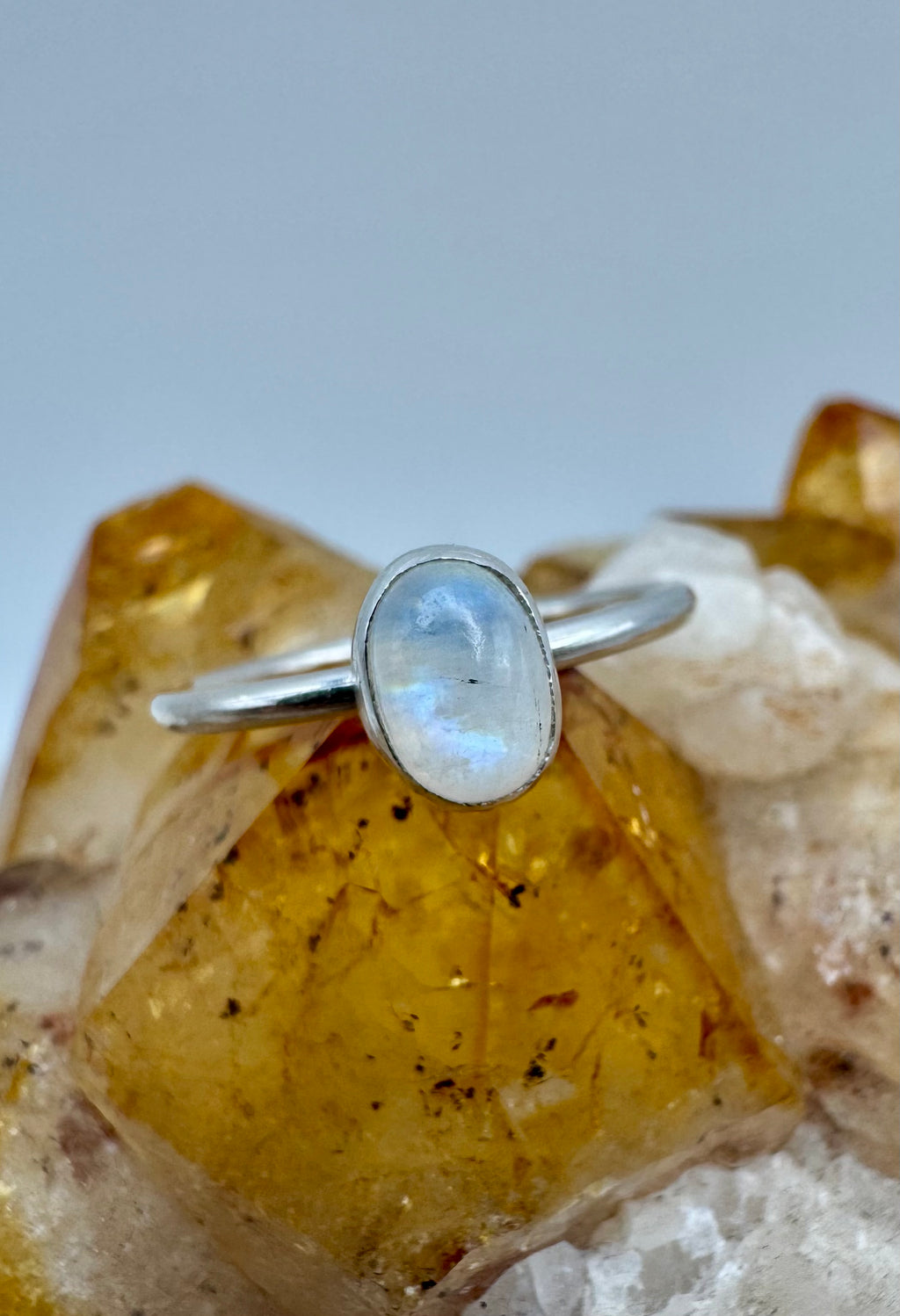 A sterling silver stacking ring with an oval moonstone cabochon, displayed on a crystal cluster against a neutral gray background.